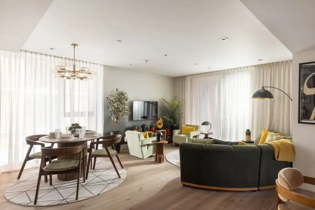 Modern bedroom with a neatly made bed, blue curtains, and a beige chaise lounge