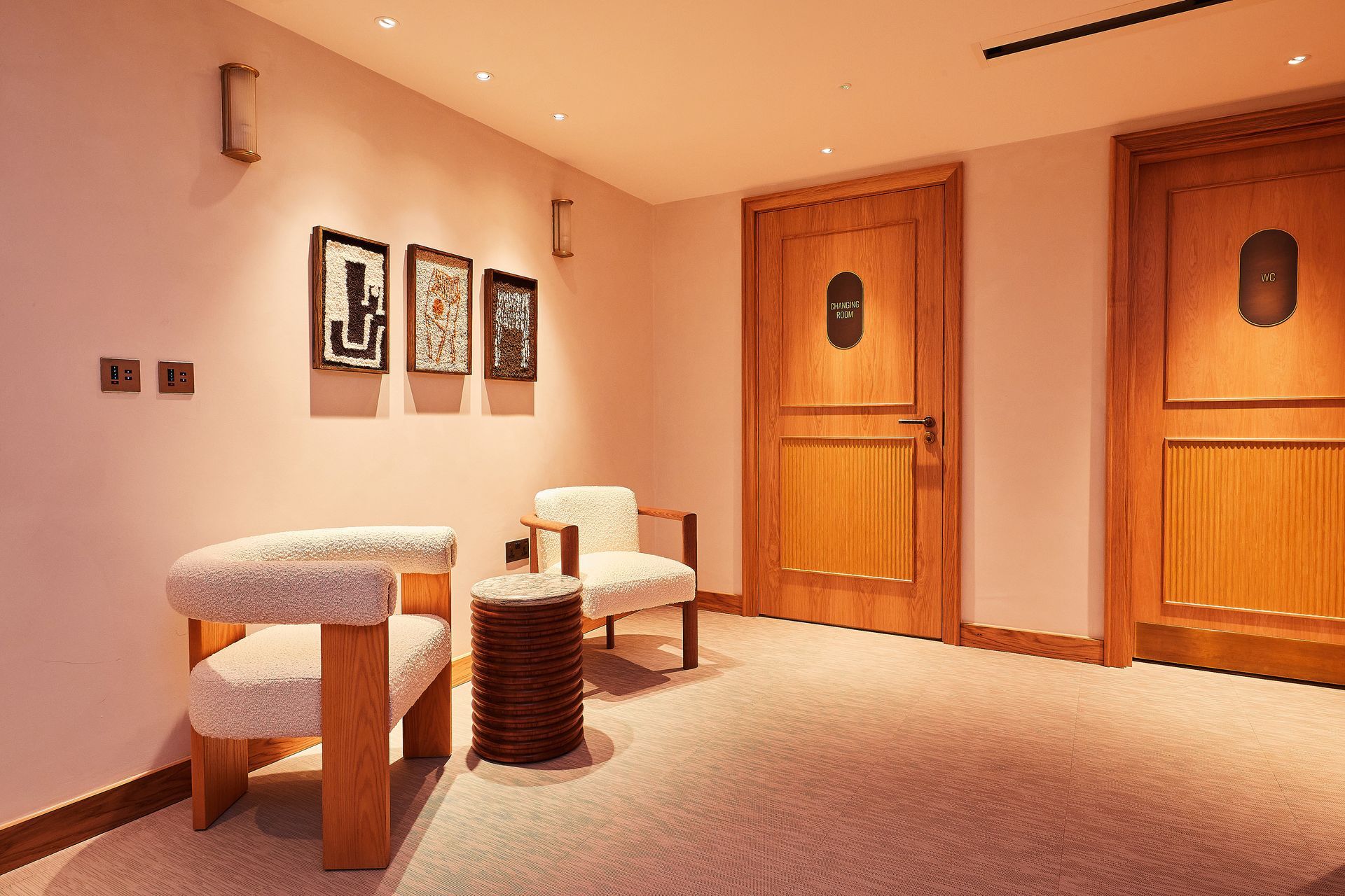 Warm spa waiting room with beige chairs, wood doors, and framed wall art