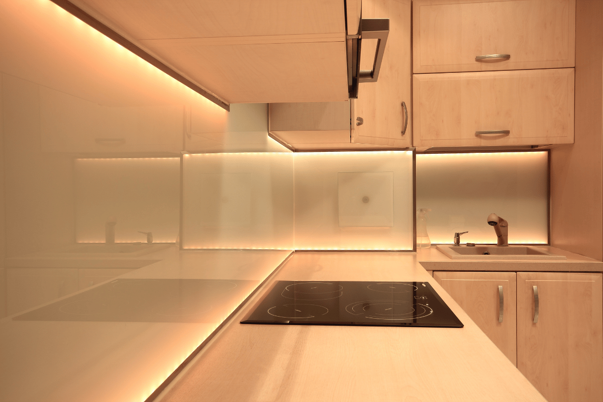 Modern kitchen with under-cabinet lighting, light wood cabinets, and white countertops.