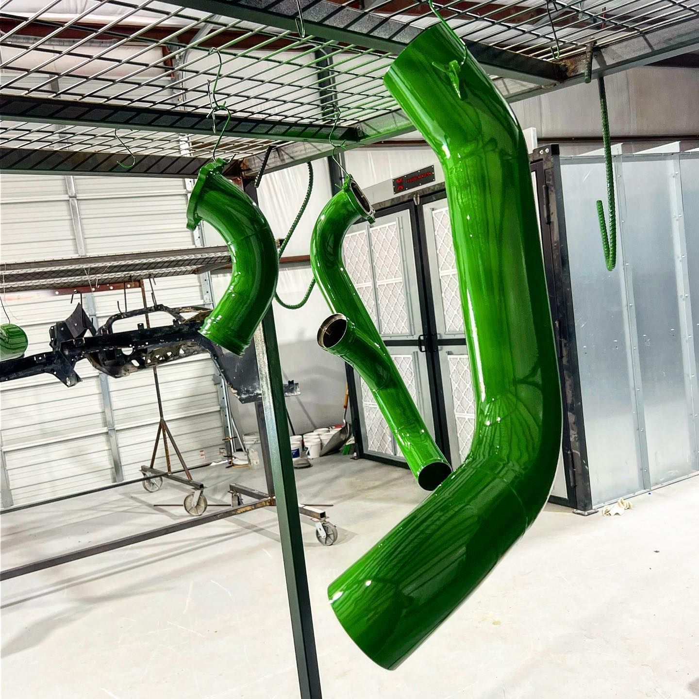 Green painted metal pipes hanging from a rack inside a workshop.