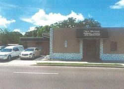 Small brick public building with parked cars in front under a blue sky.