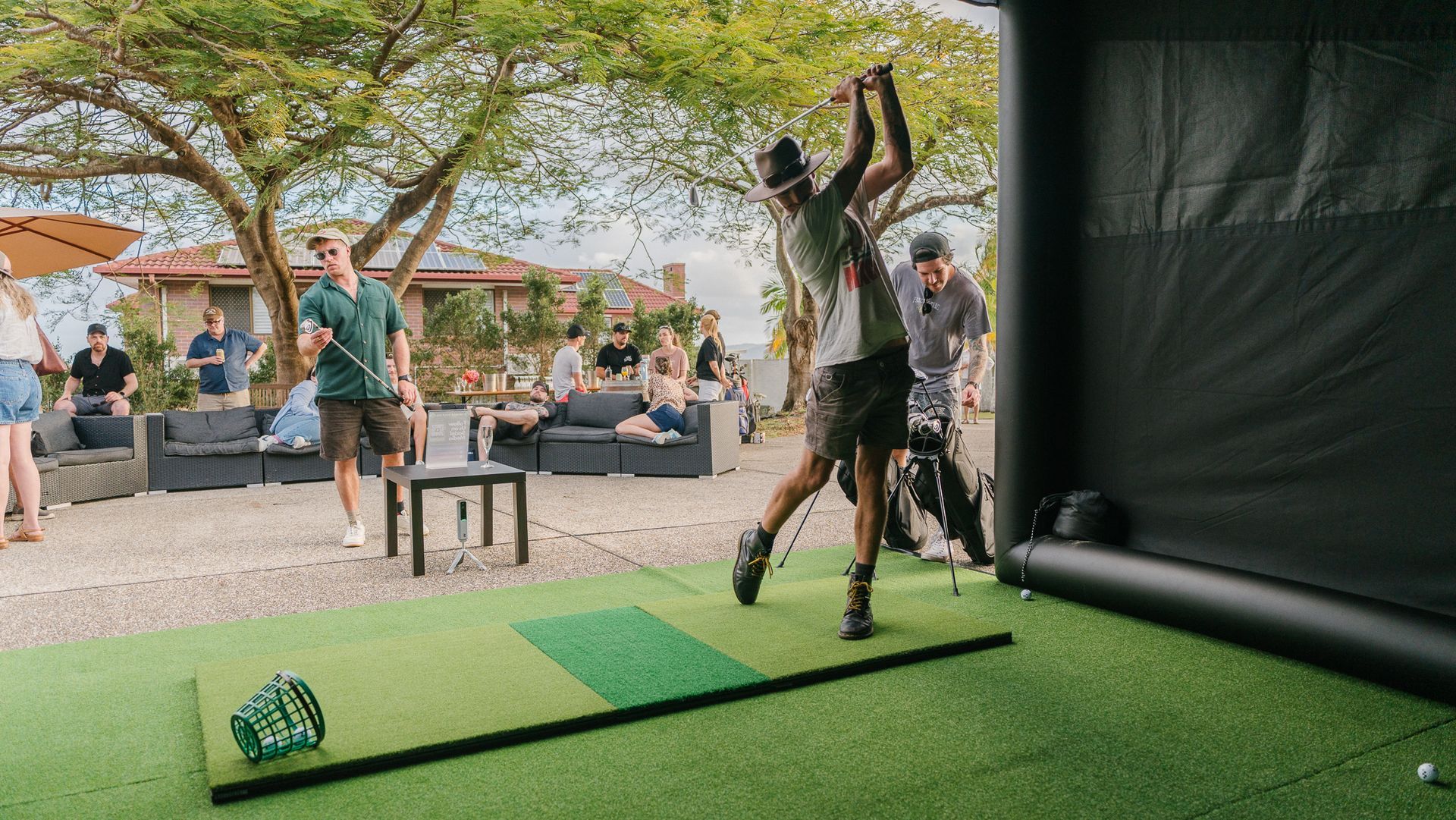 Portable golf simulator with a golfer swinging inside, audience seated in the background.