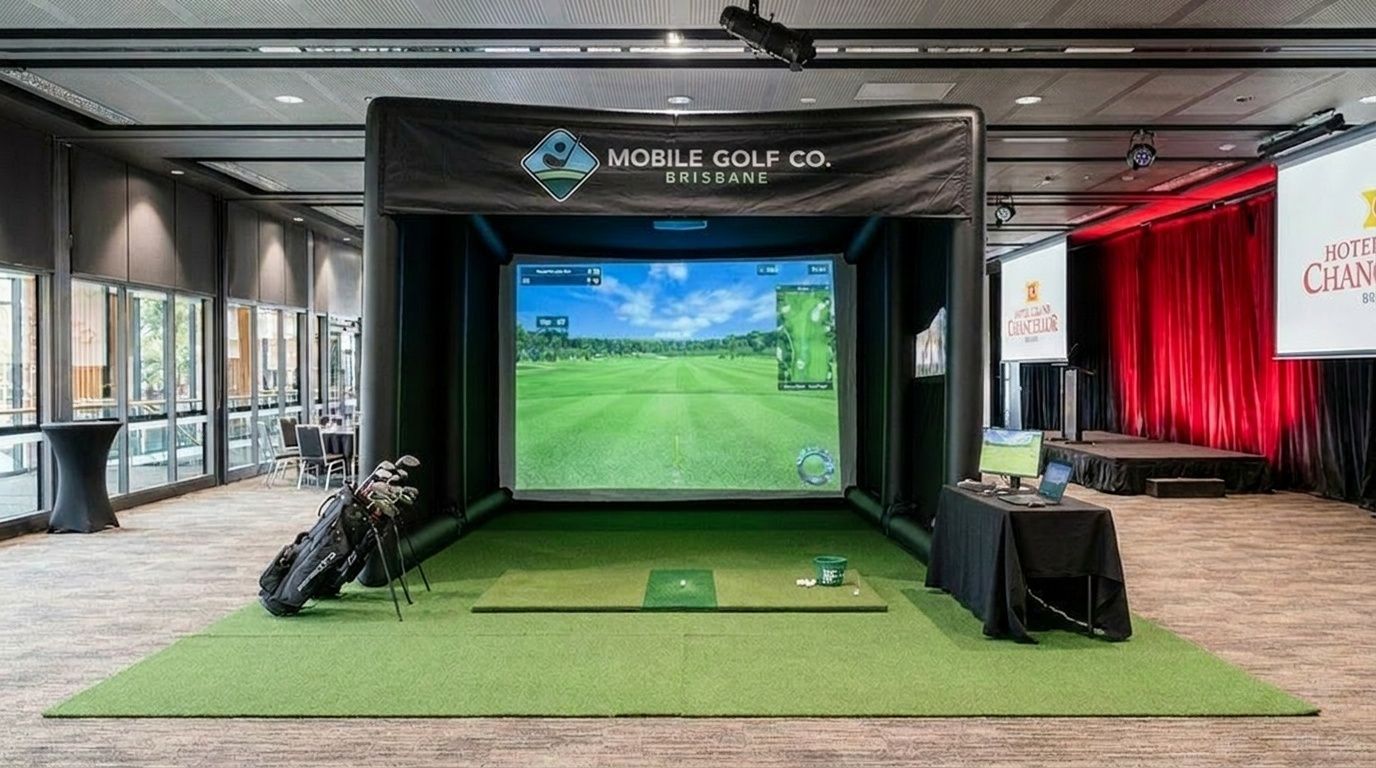 Indoor golf simulator booth with a large screen, green turf, and golf clubs in a conference hall.