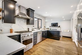 Modern kitchen with dark cabinets, white marble countertops, stainless steel appliances, and wood floors.