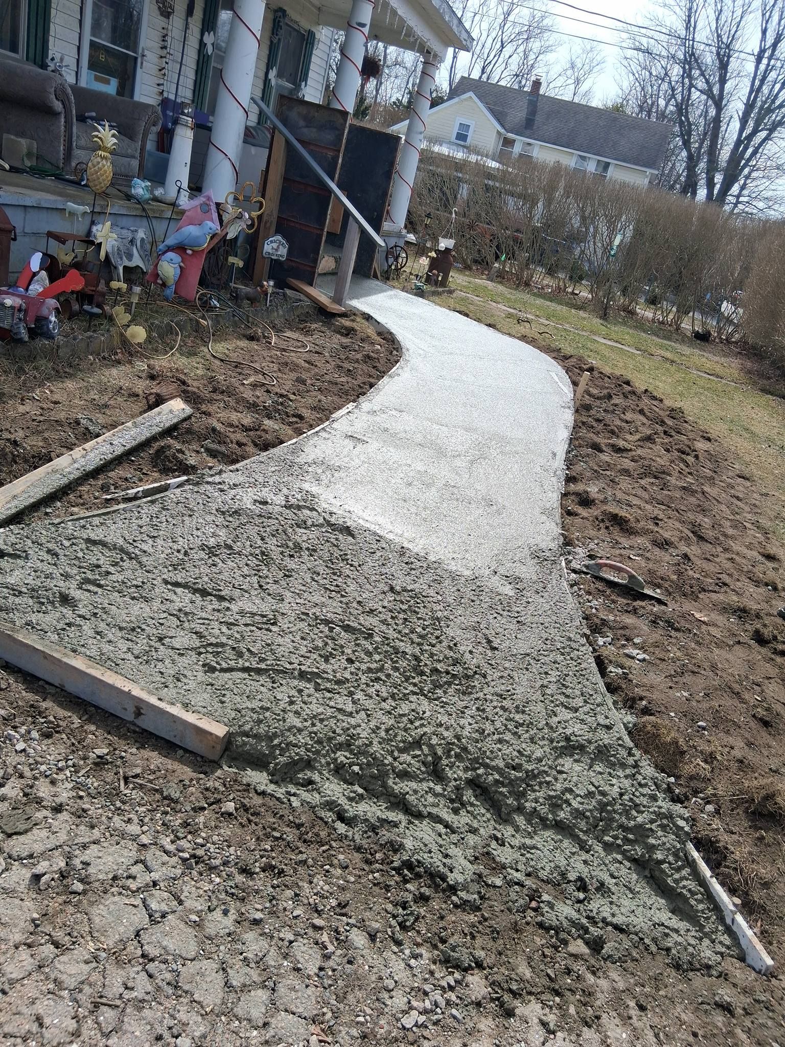 A freshly poured concrete walkway leading to a house entrance, framed by wooden boards on dirt ground.