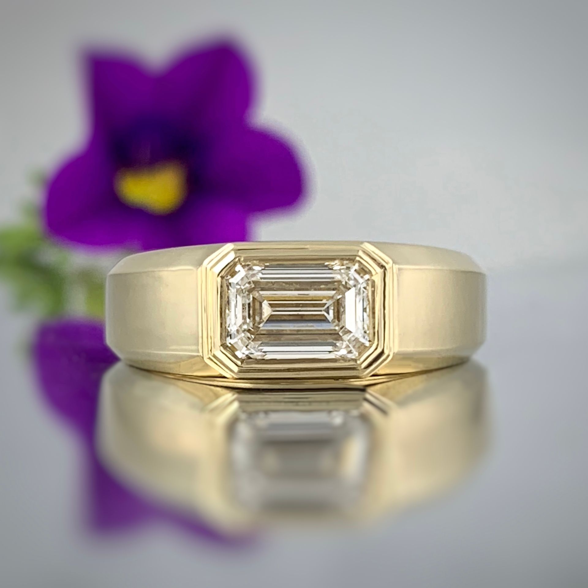 A diamond ring is reflected in a mirror with a flower in the background