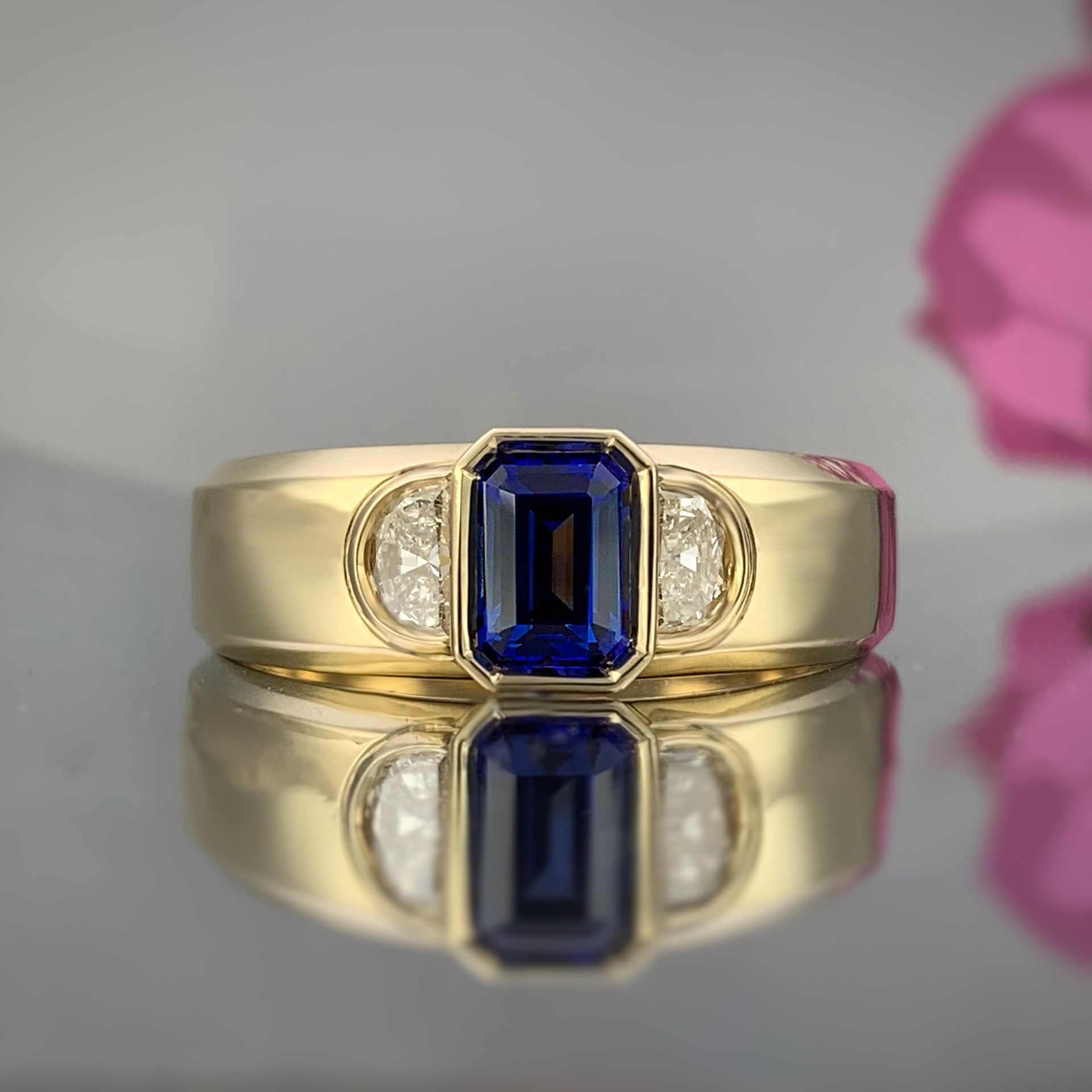 A yellow gold ring with a sapphire and diamonds on a table.