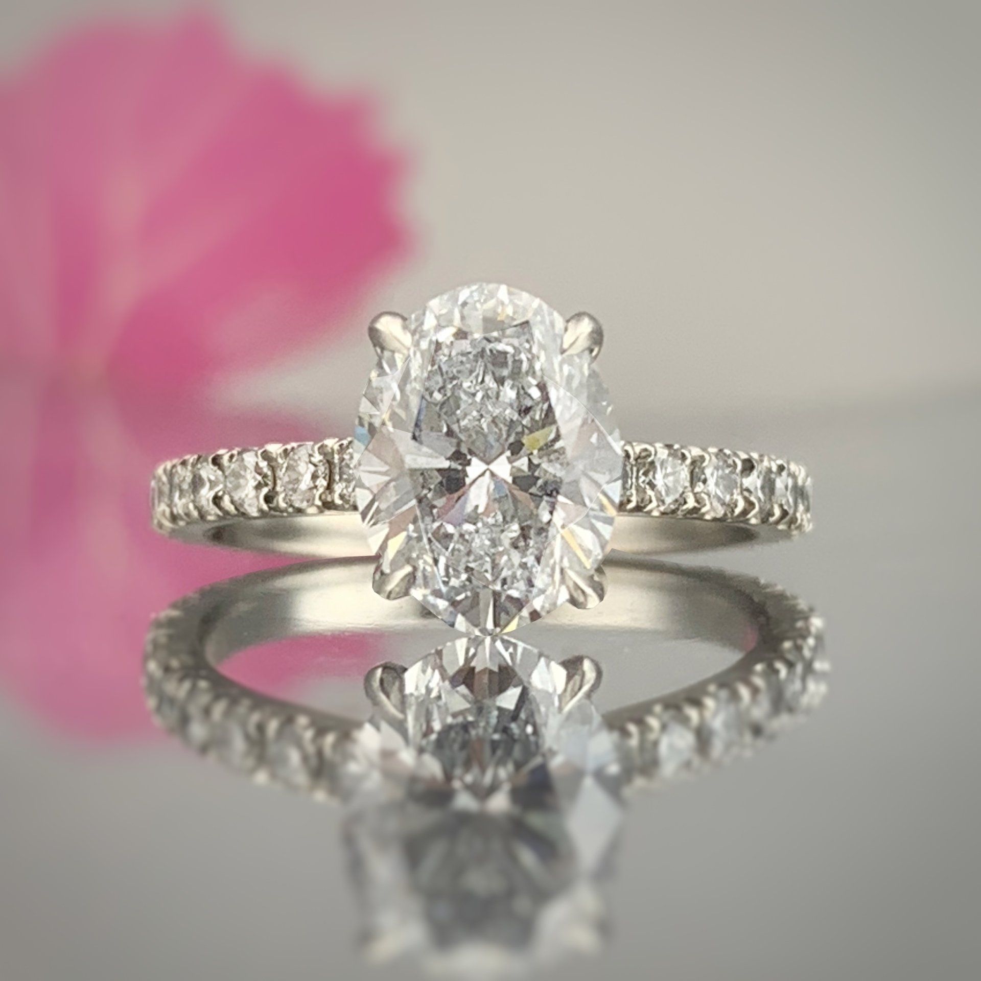 A diamond ring is sitting on a table next to a pink flower.