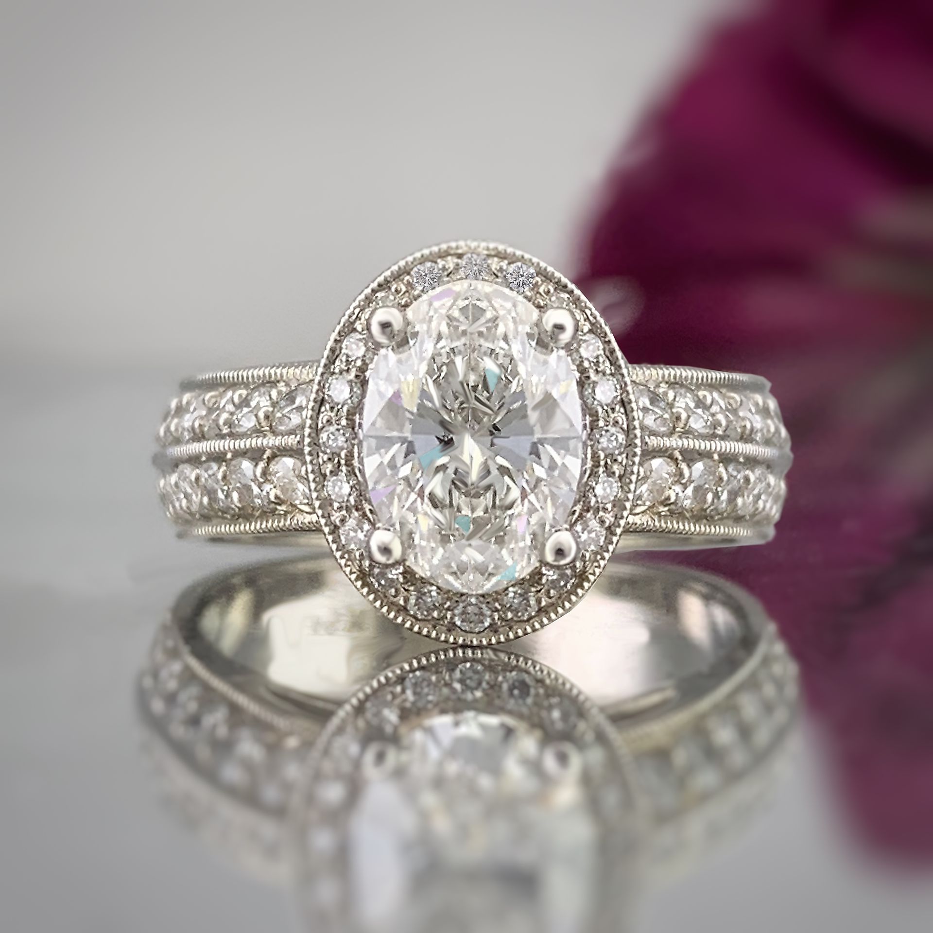 A diamond ring is sitting on a table next to a purple flower.