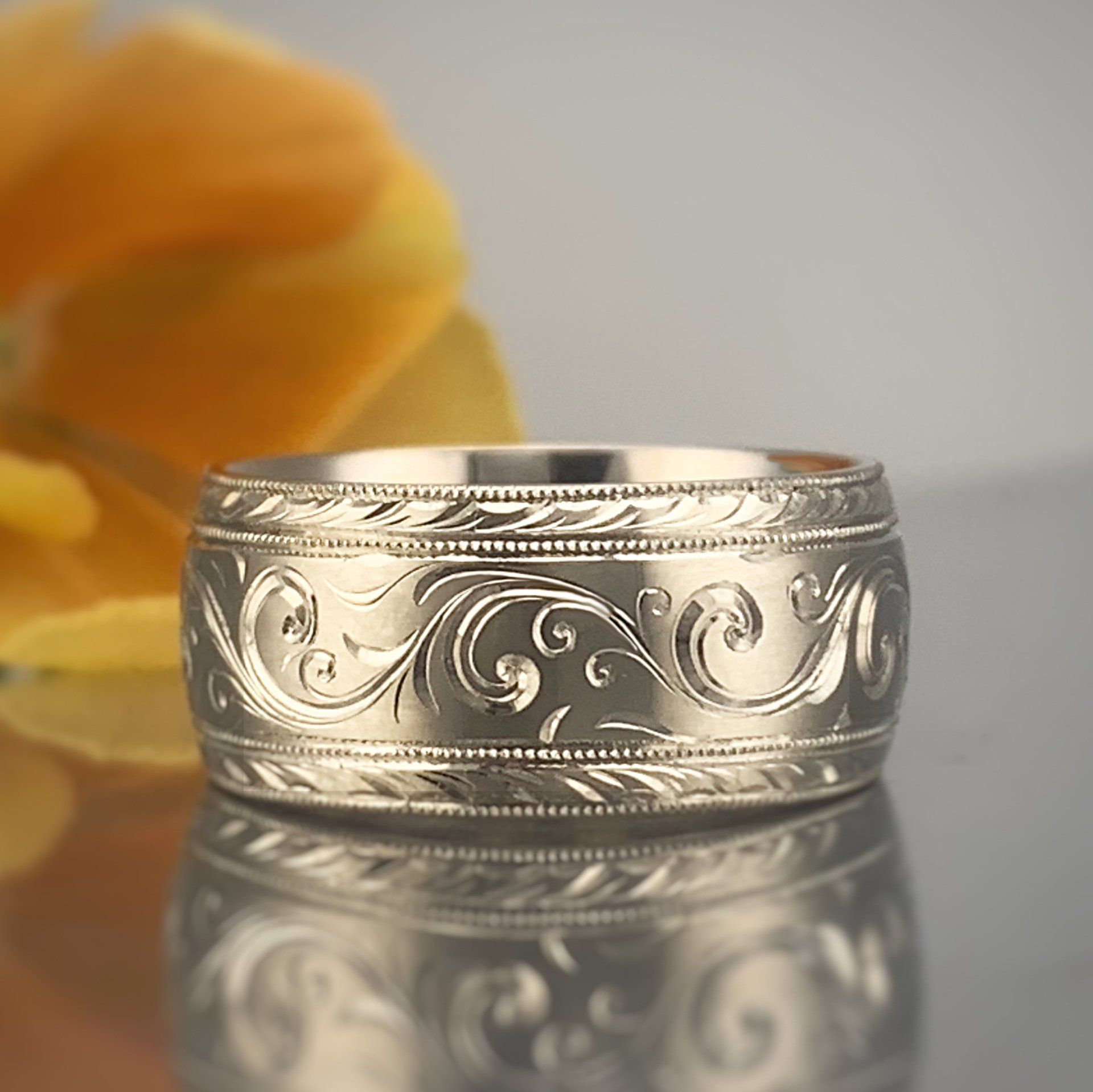 A silver ring is sitting on a table next to a flower.