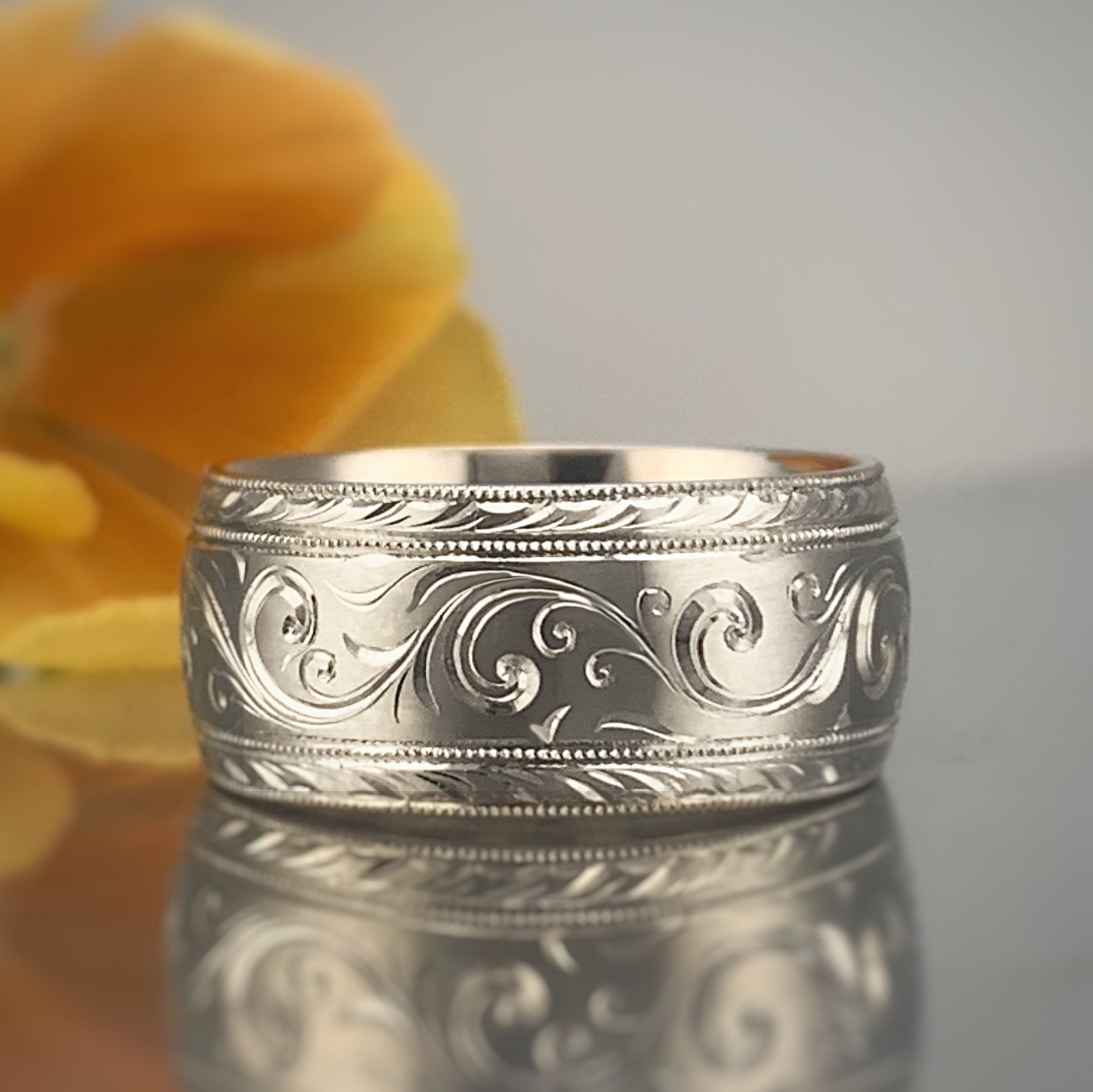 A silver ring is sitting on a table next to a flower.