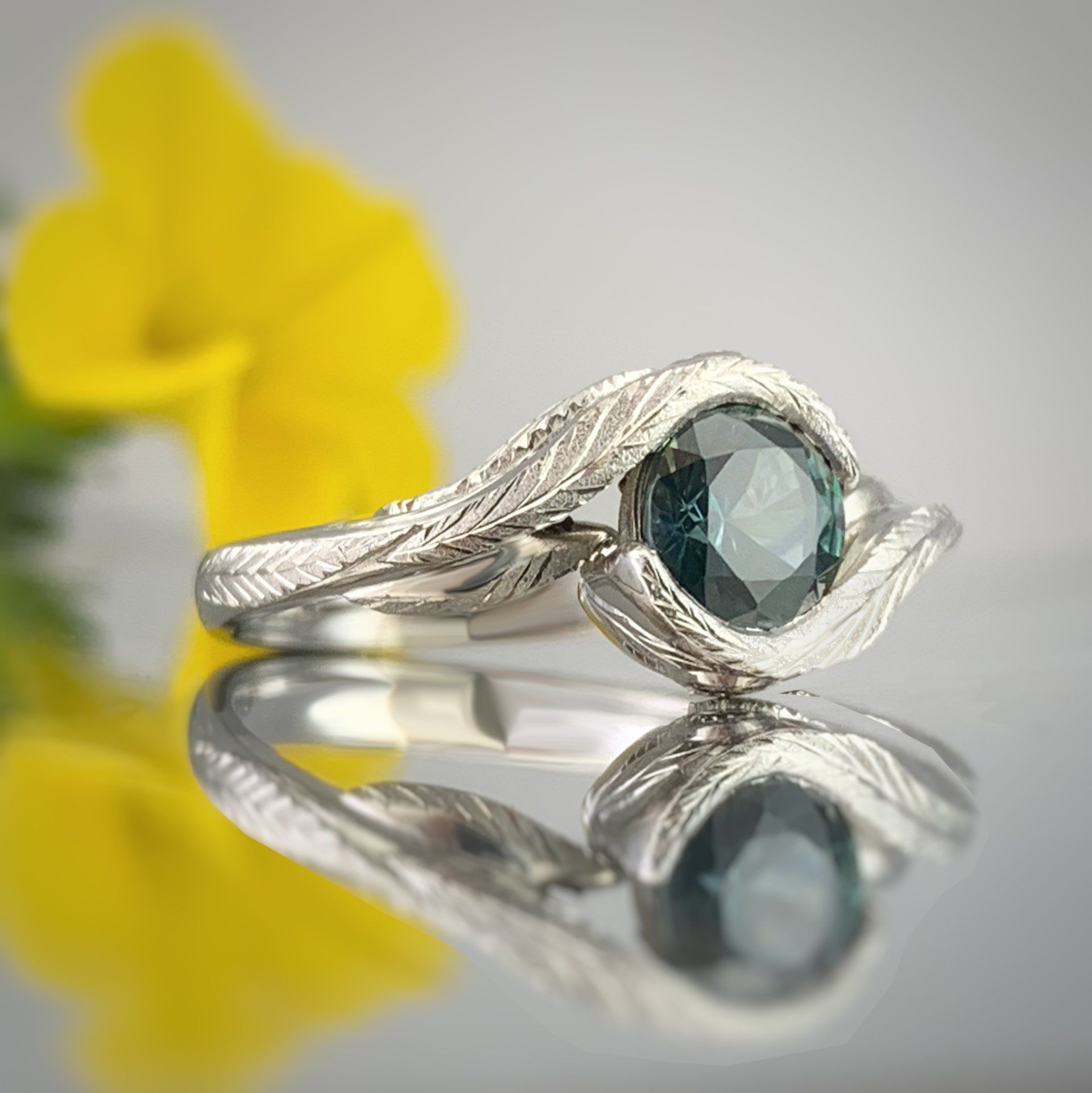 A close up of a ring on a table with a yellow flower in the background.