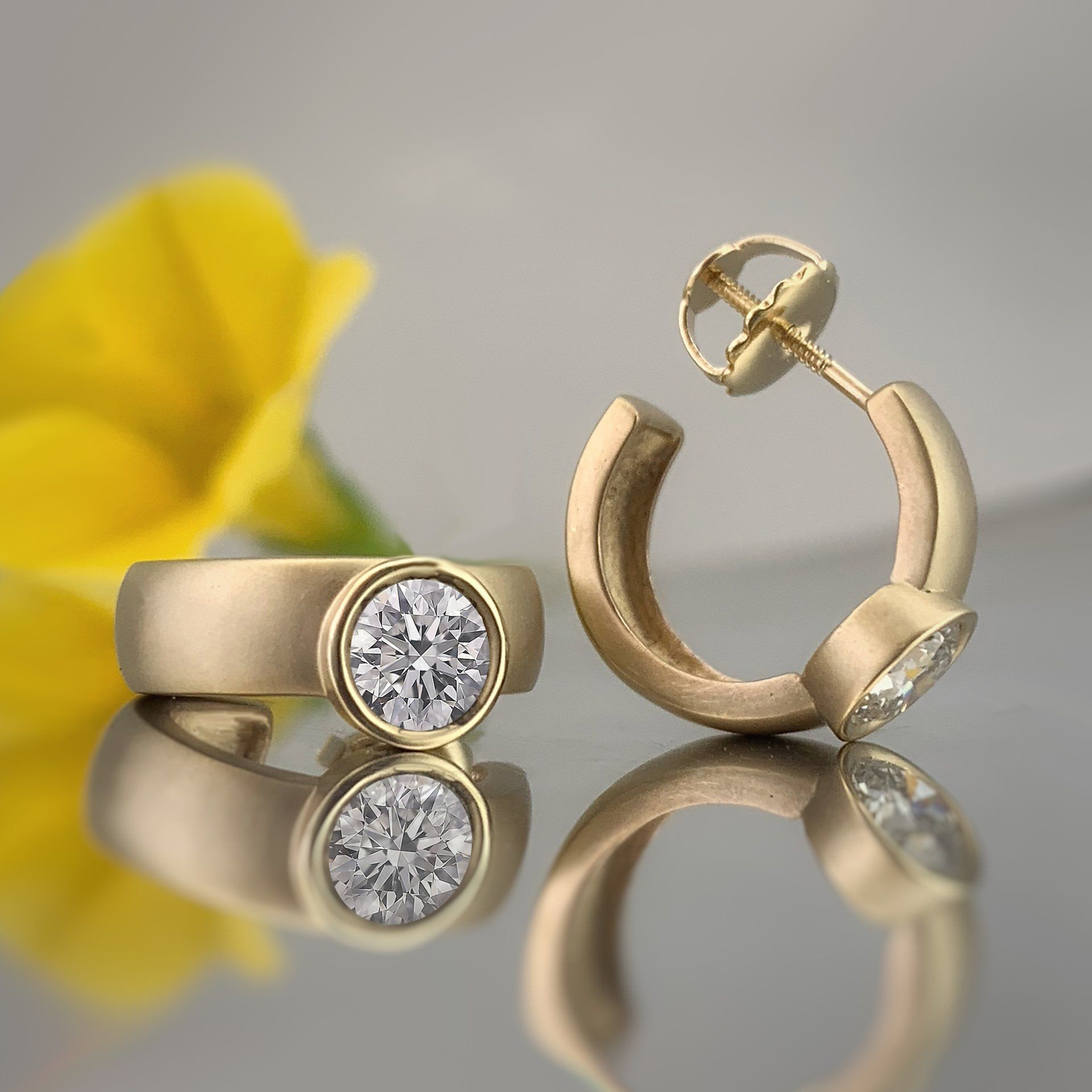 A pair of earrings and a ring are on a table with a yellow flower in the background