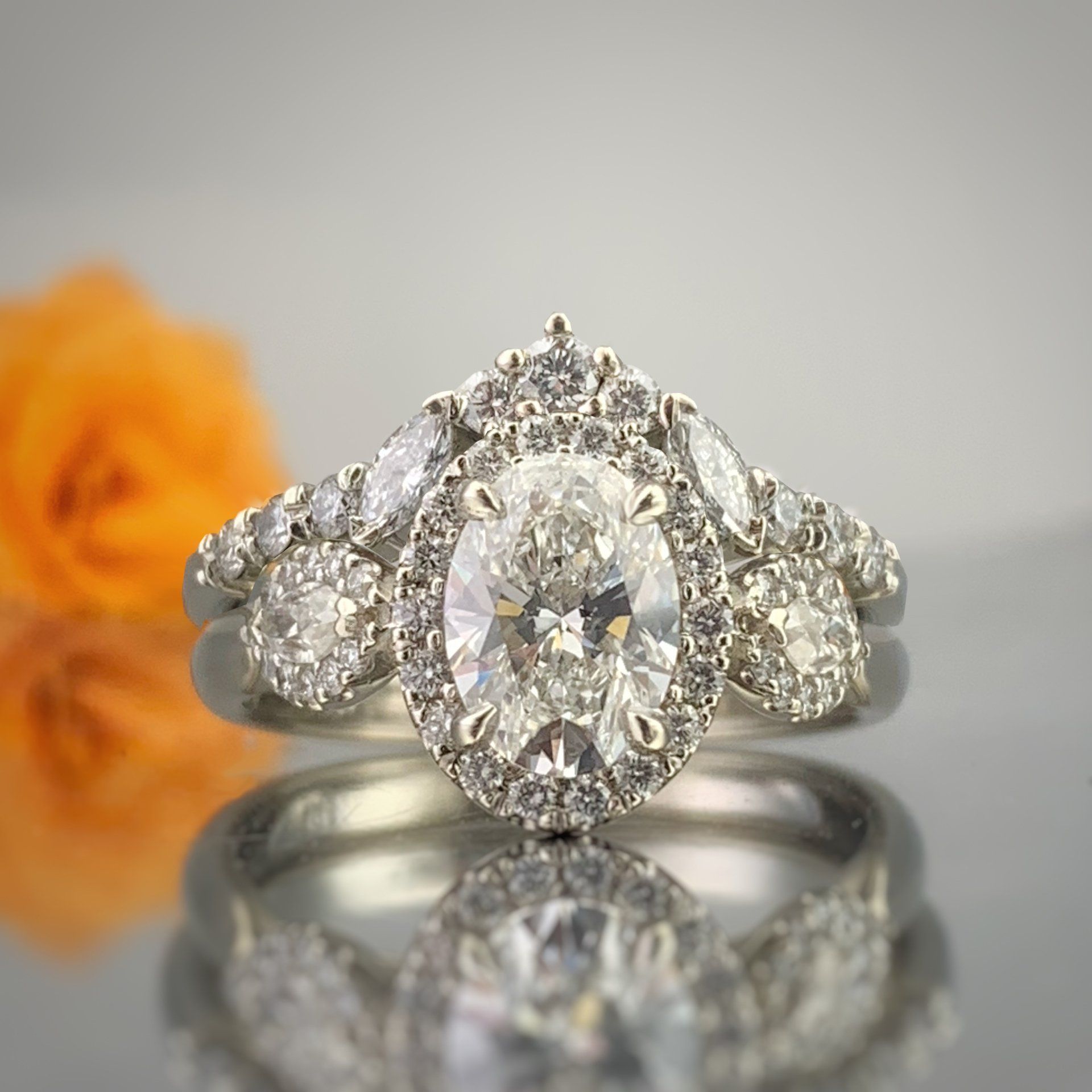 A diamond ring is sitting on a table next to a flower.