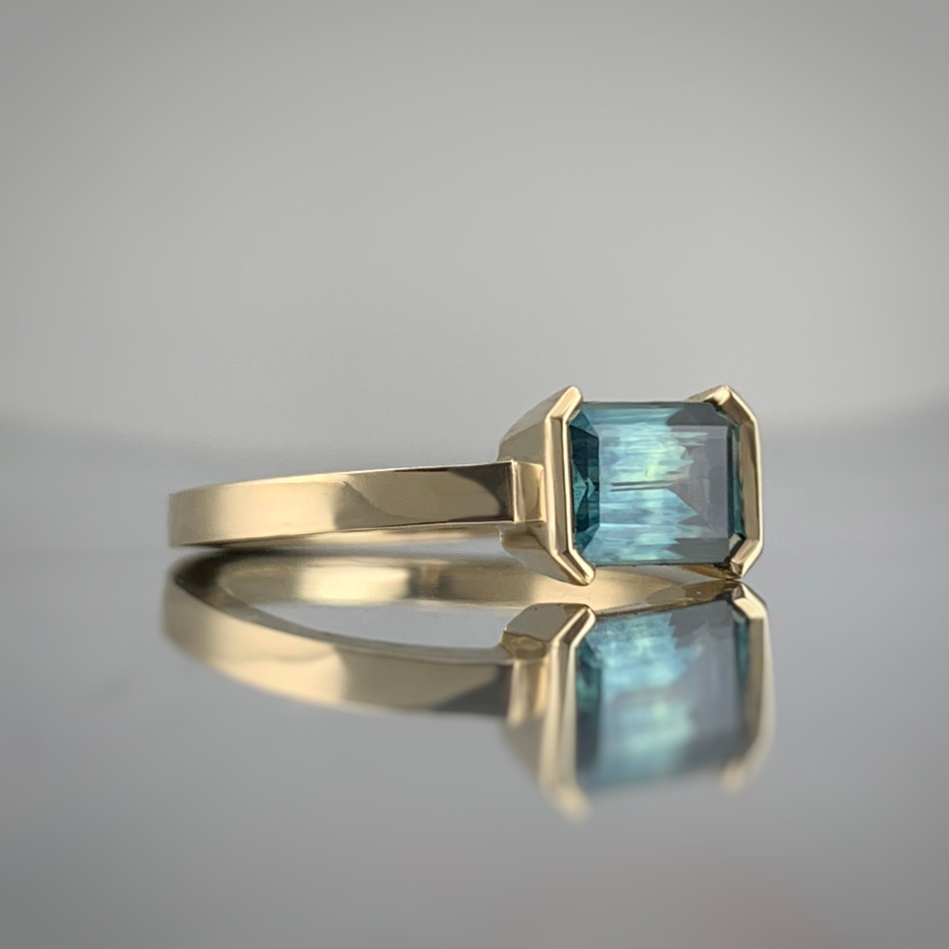 A gold ring with a blue stone in it is sitting on a table.