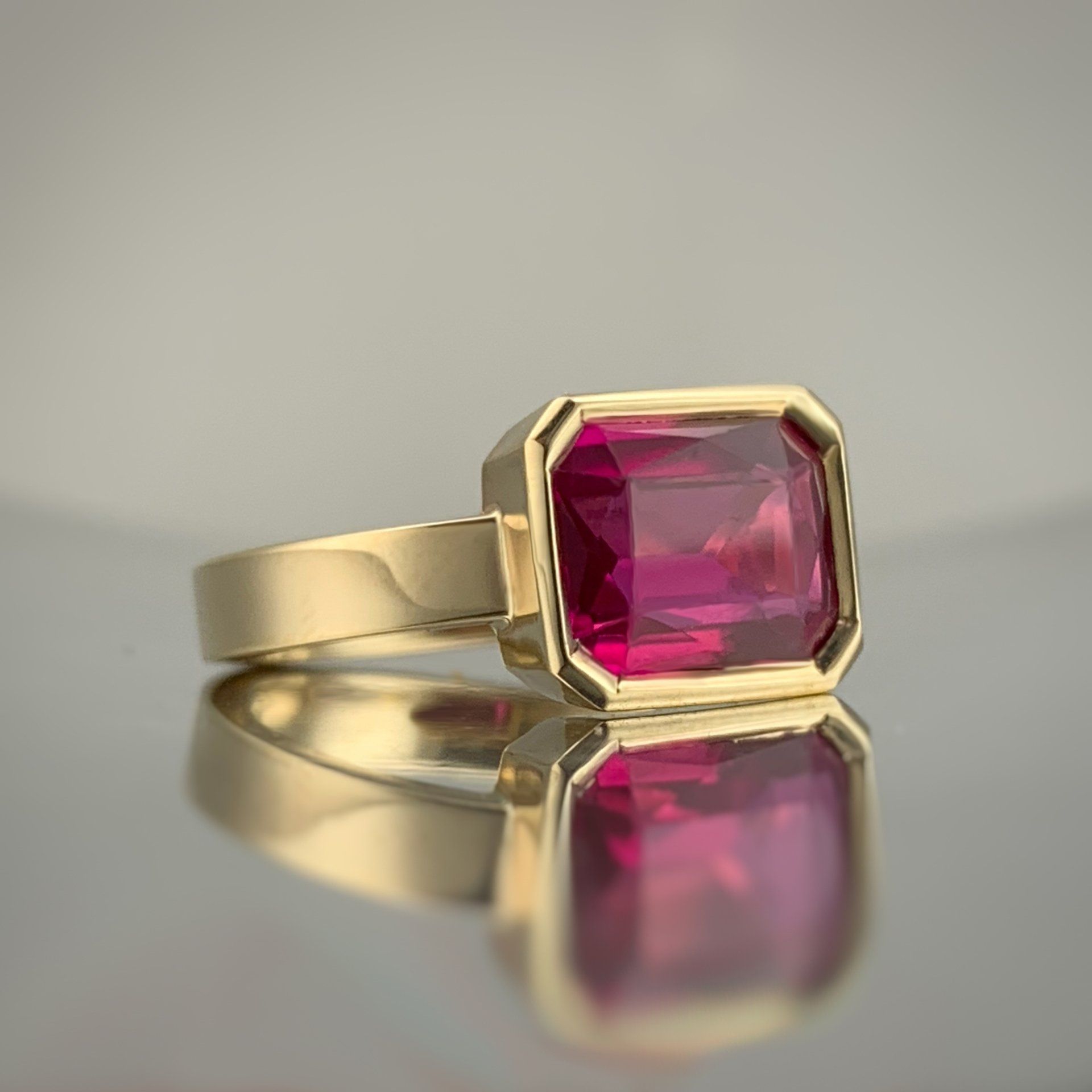 A gold ring with a pink stone in it is sitting on a table.