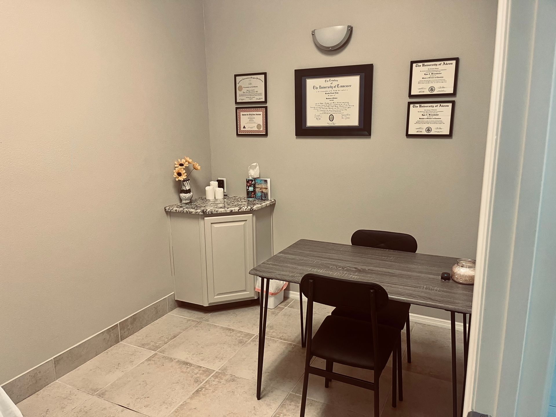 Small office with a table and chairs, framed certificates on the wall, and a cabinet with supplies.
