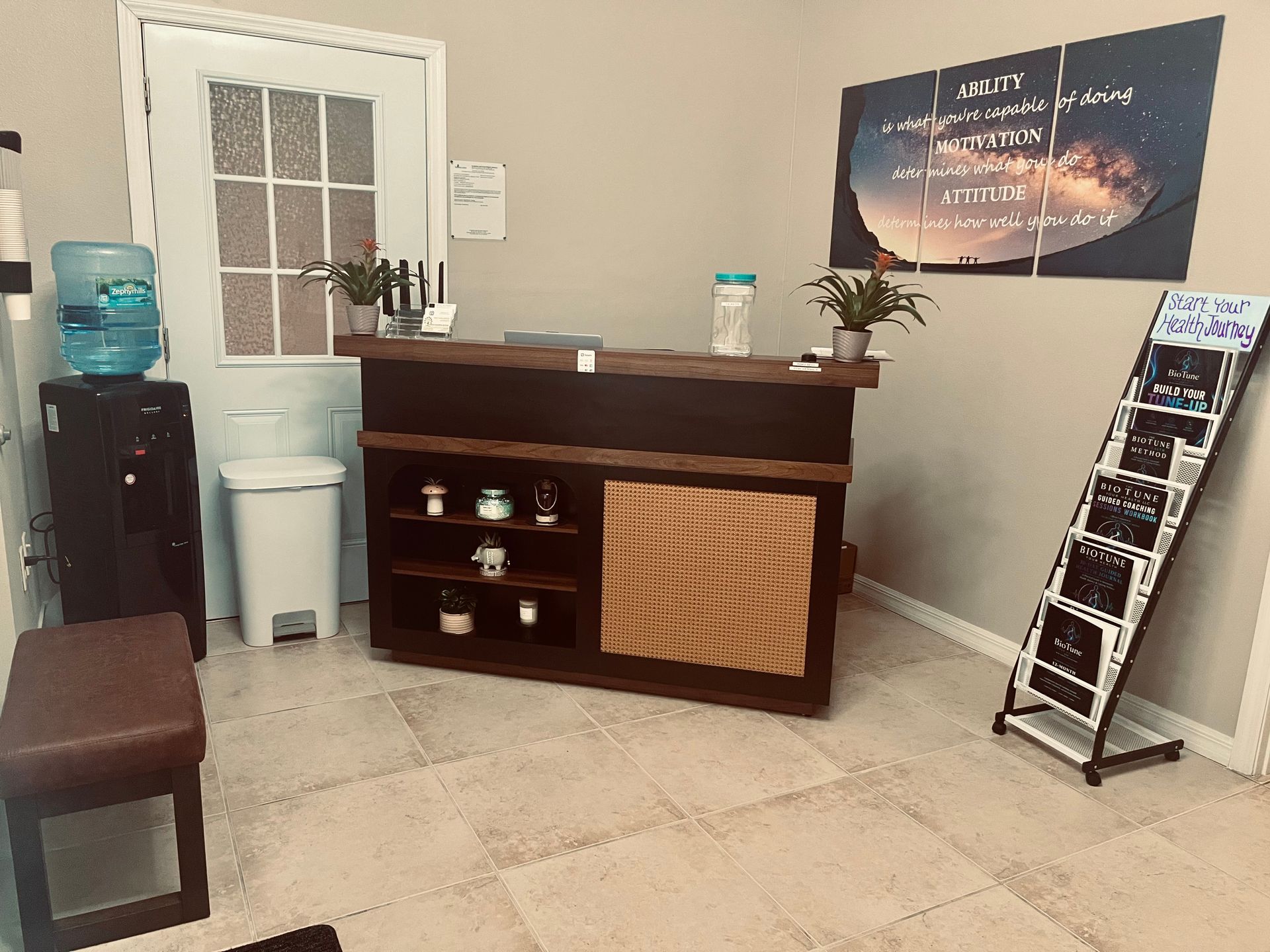 Reception desk in a small office lobby with beige tile floors, water cooler, and brochure stand