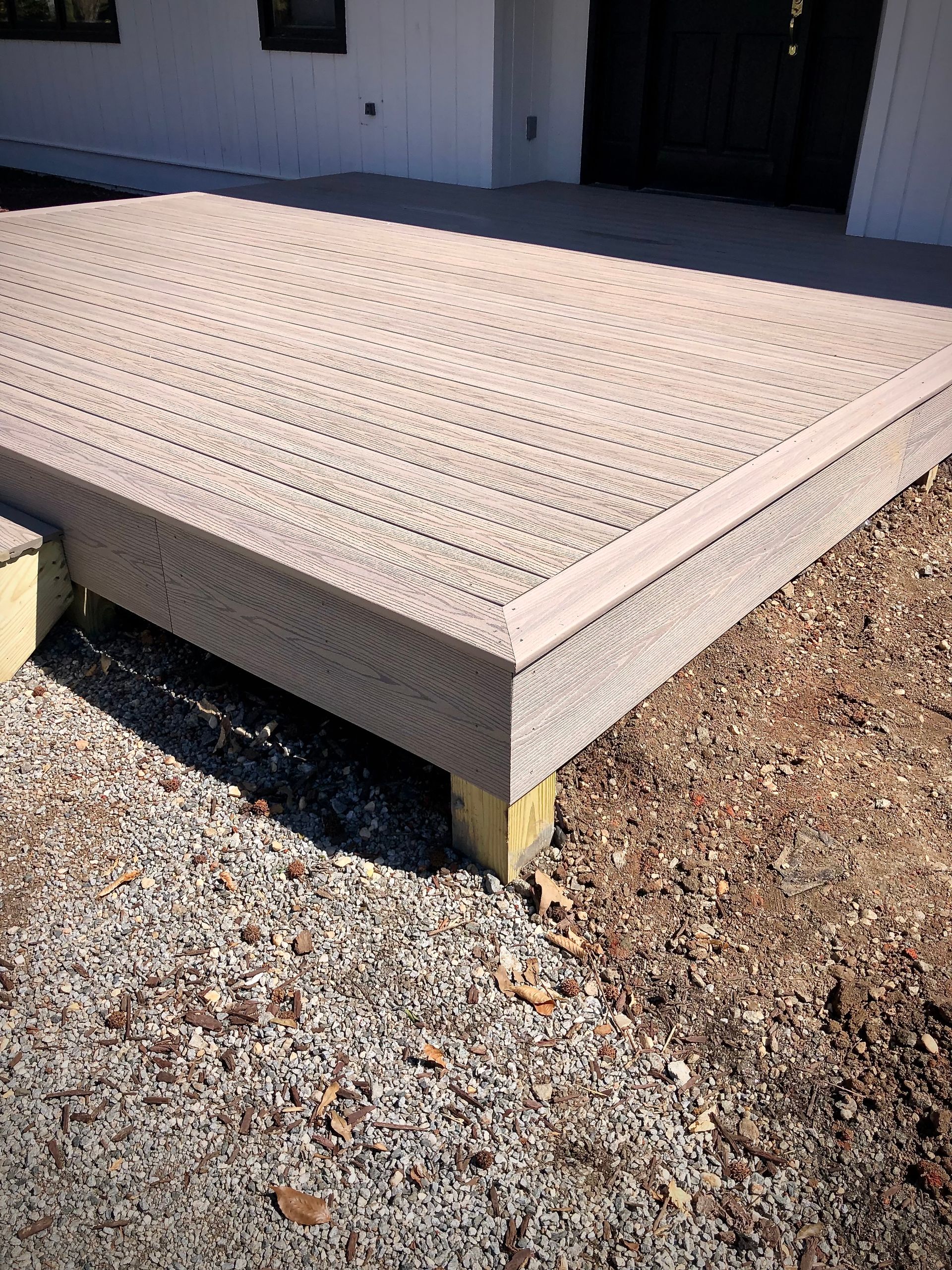 A wooden deck is sitting on top of gravel in front of a house.