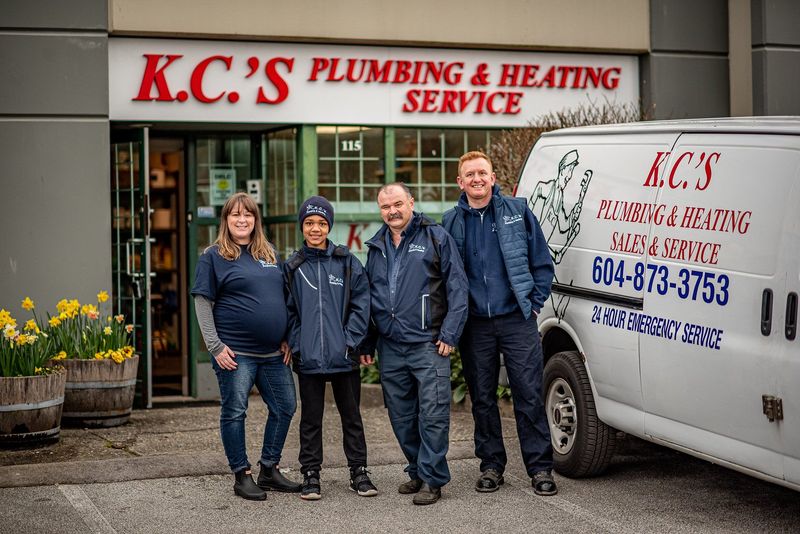 Four people stand beside a K.C.’s Plumbing & Heating Service van in a driveway.