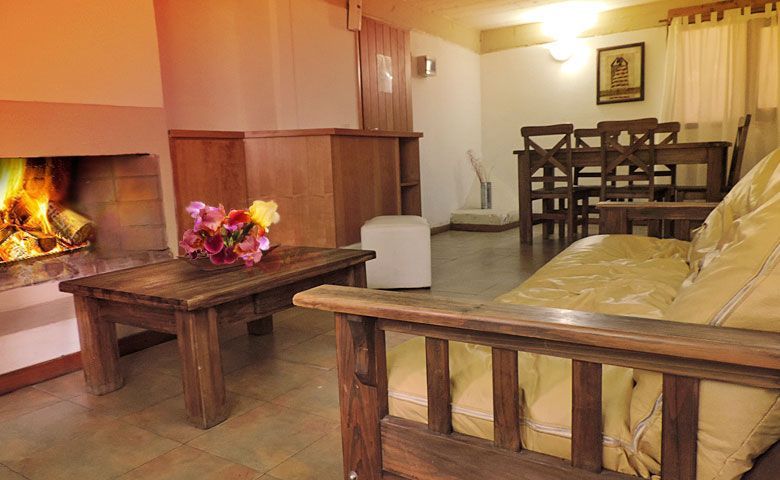 Acogedora sala de estar con chimenea, muebles de madera, sofá amarillo y mesa de comedor al fondo.