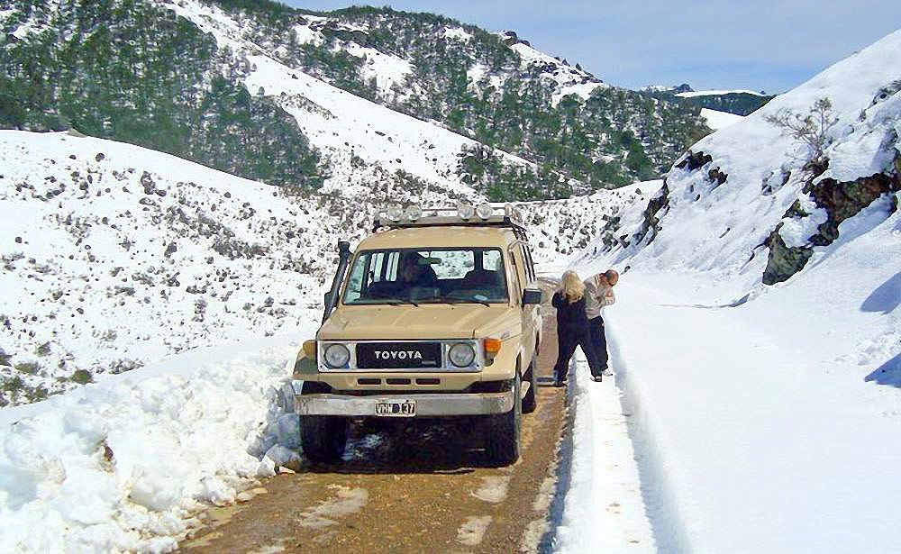 Camioneta color canela en una carretera de montaña nevada con una persona de pie a su lado.