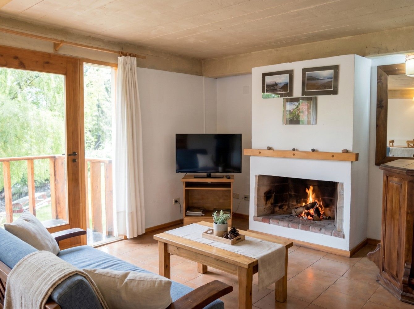 Acogedora sala de estar con chimenea, televisor, mesa de centro y puerta corredera que da a un balcón.