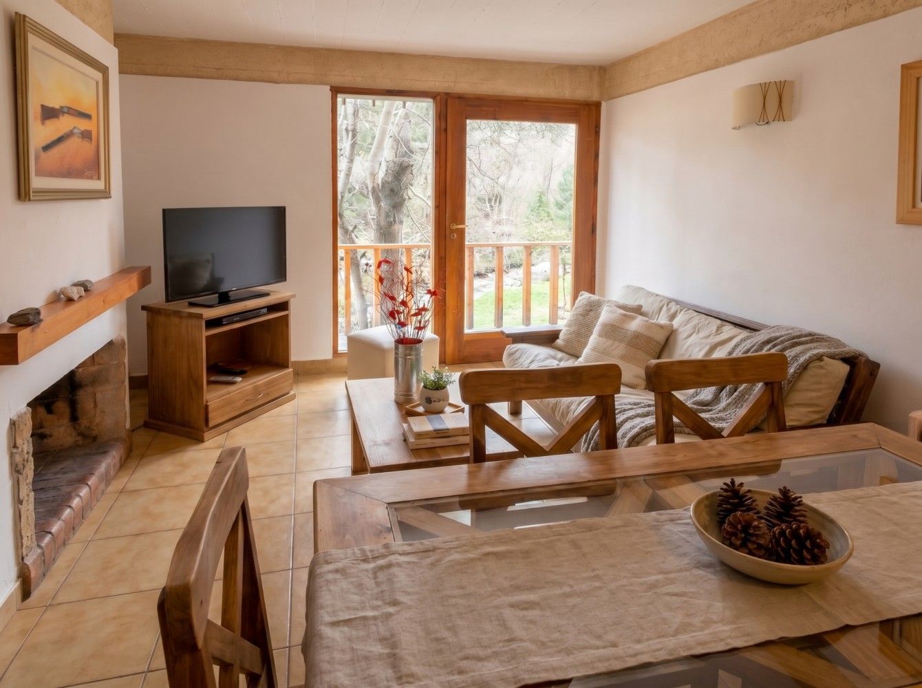 Acogedora sala de estar con sofá, televisor, chimenea y puertas que dan al balcón con vistas a los árboles.