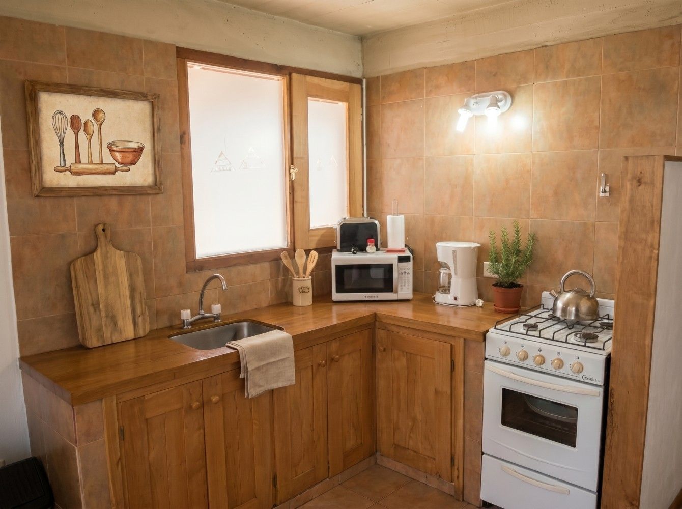 Pequeña cocina rústica con armarios de madera, estufa blanca, fregadero, microondas y una ventana sobre la encimera.