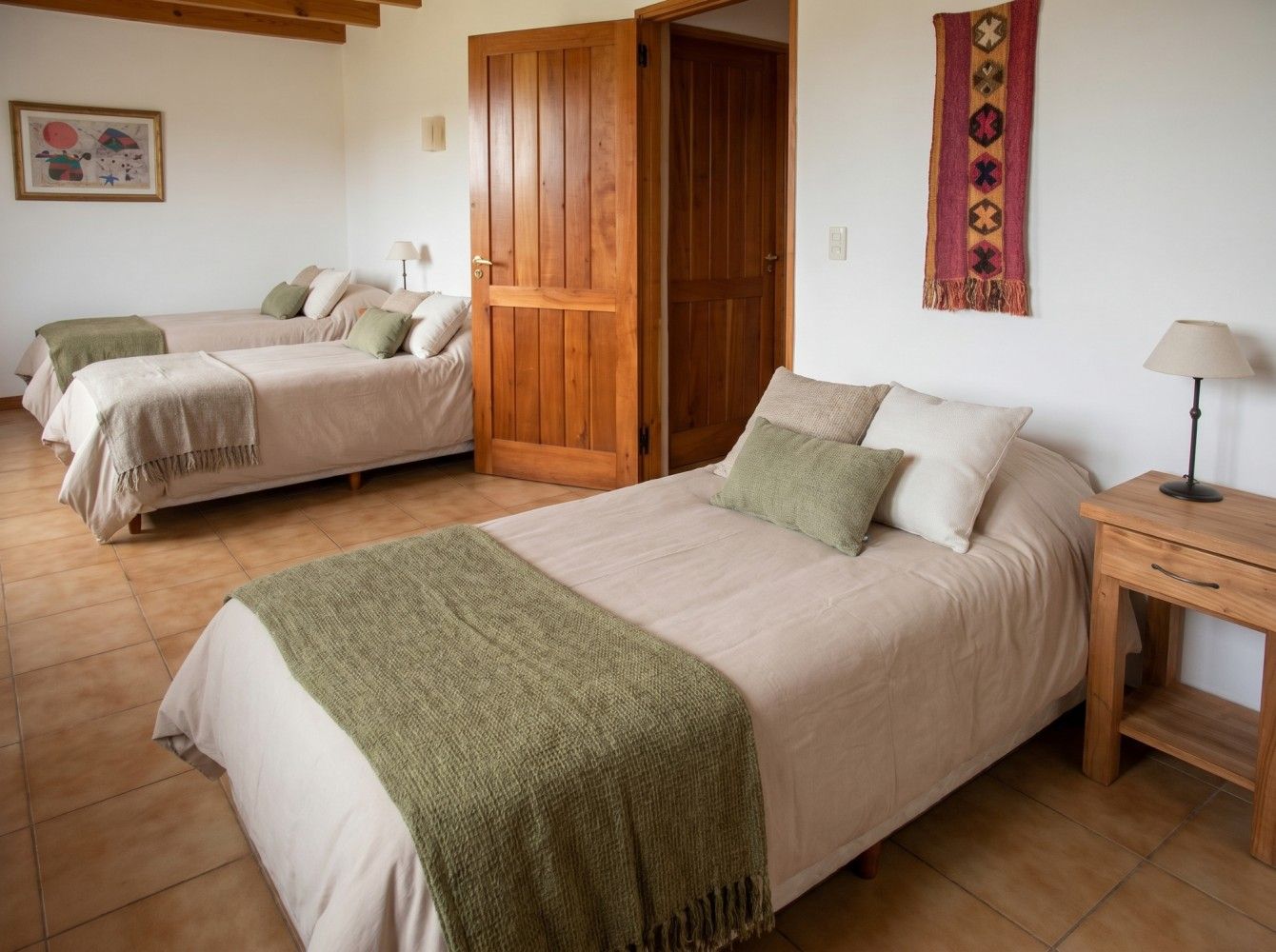Habitación con dos camas individuales, armario de madera y decoración rústica en una estancia luminosa.