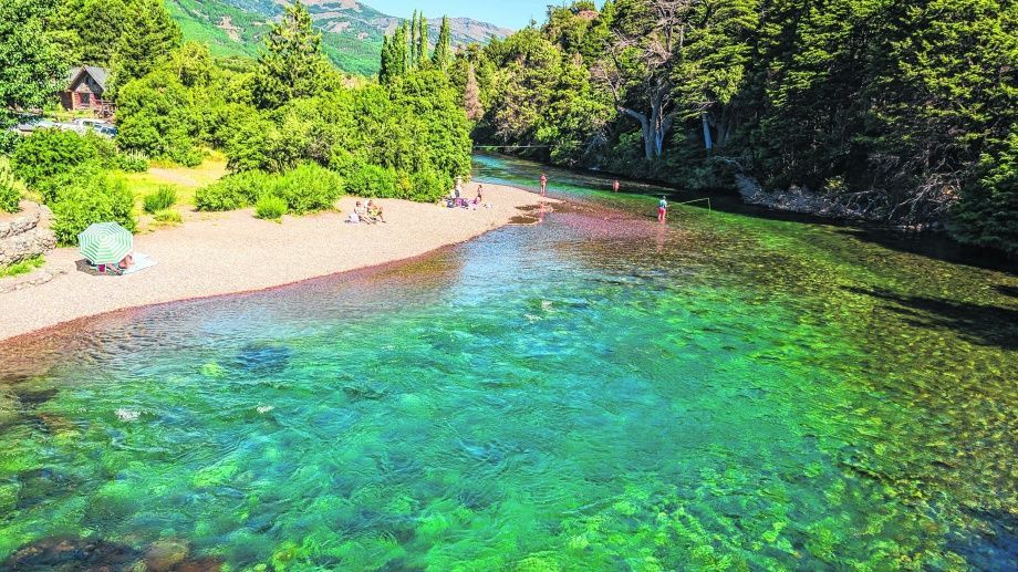 Un río de aguas cristalinas color turquesa junto a una playa de arena y un frondoso bosque verde en un día soleado.