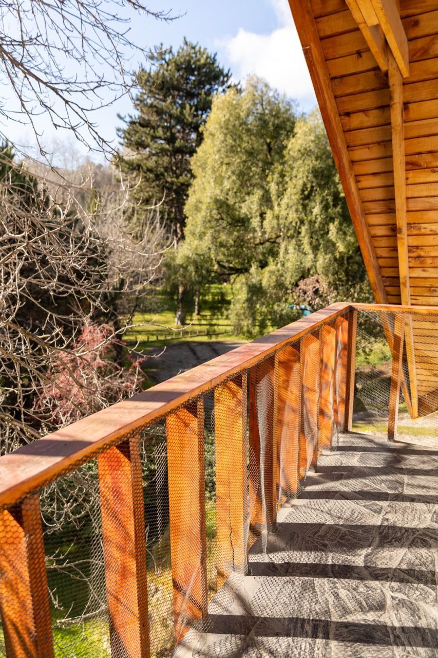 Balcón de madera con barandilla naranja con vistas a un jardín soleado y árboles.