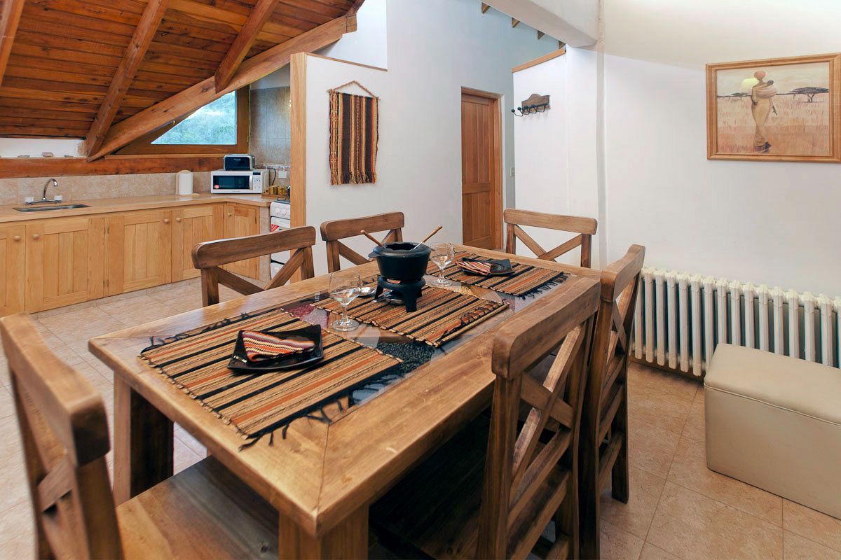 Mesa de comedor rústica con vajilla en una acogedora buhardilla con vigas de madera, paredes blancas y un radiador.
