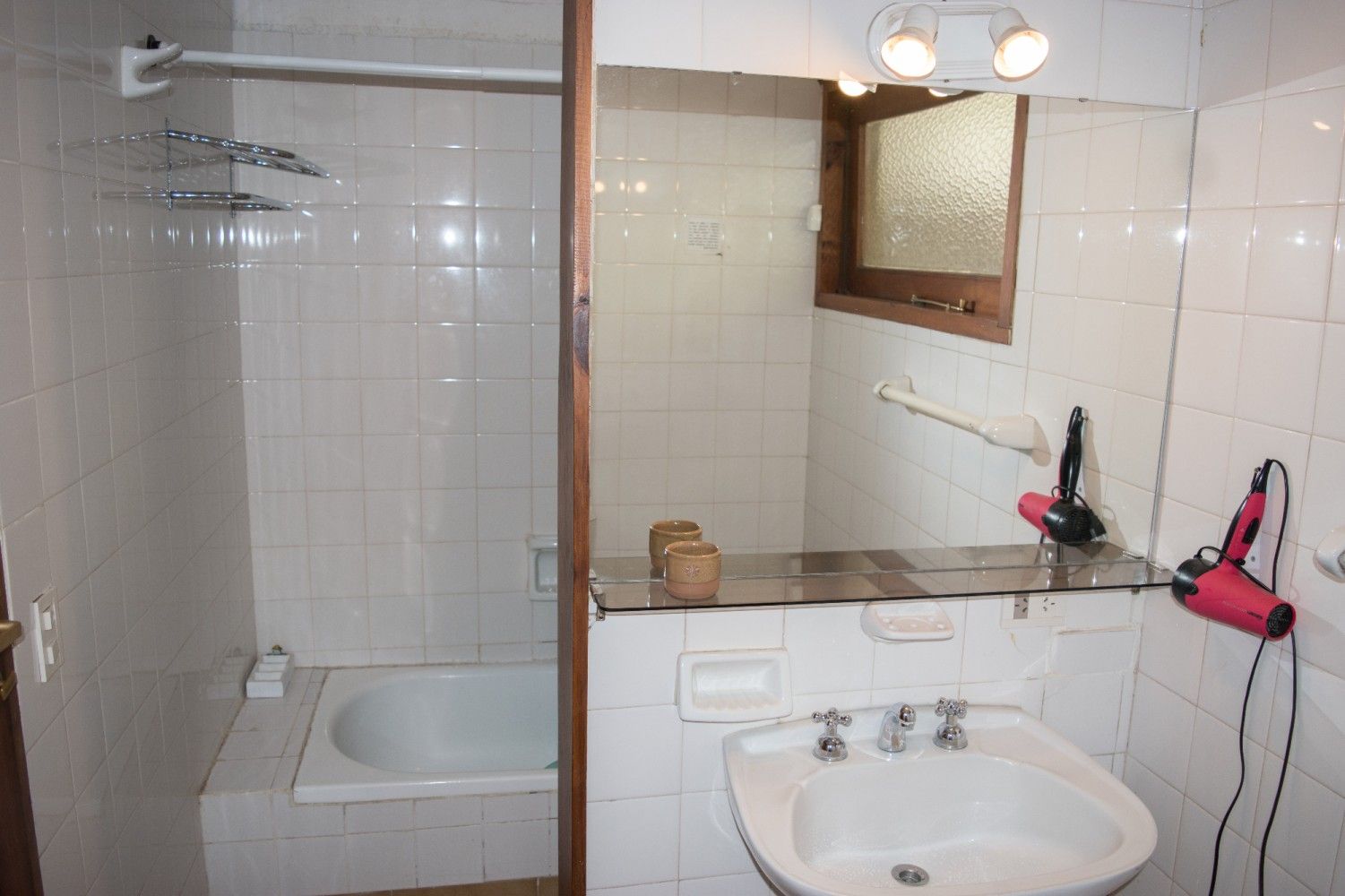 Baño pequeño con bañera, lavabo, espejo y paredes alicatadas en blanco.