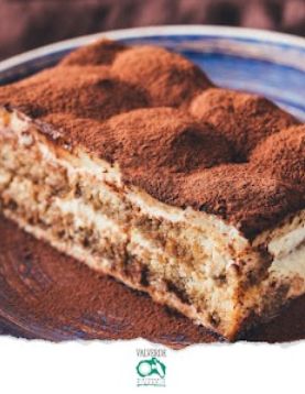 Una fetta di tiramisù su un piatto, spolverata di cacao in polvere.