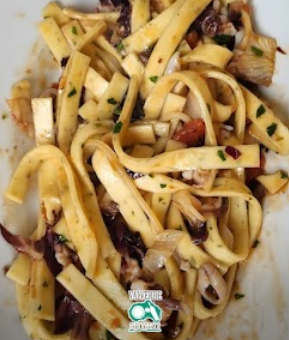 Piatto di pasta con erbe aromatiche, pezzetti di pomodoro e un sugo leggero.