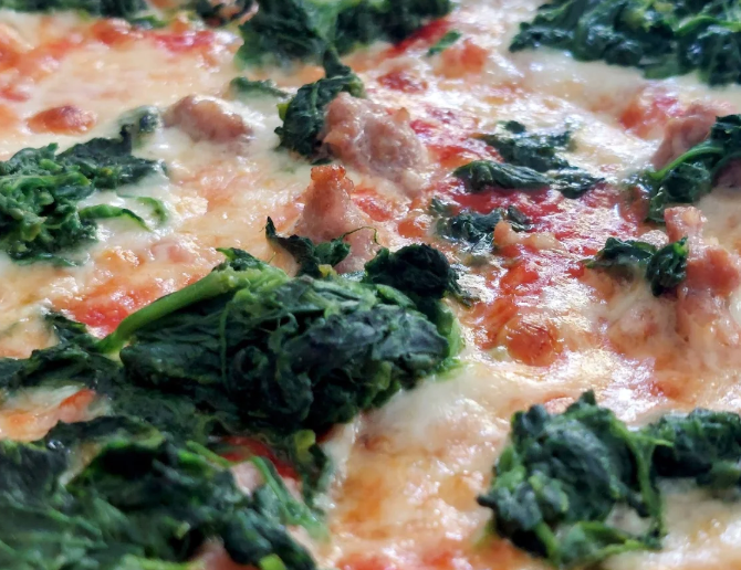 Primo piano di una pizza con spinaci e pomodoro ripiena di formaggio o di un piatto al forno.