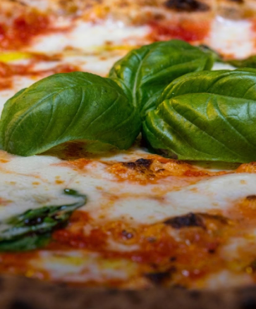 Primo piano di una pizza guarnita con foglie di basilico fresco e formaggio fuso.