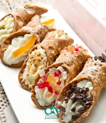 Cannoli farciti con crema, frutta, noci e cioccolato, serviti su un vassoio bianco.