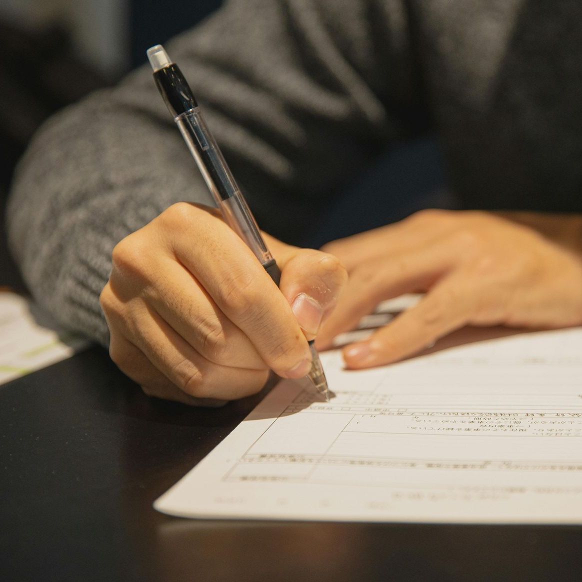 PHoto of hands of a a person holding a pen writing