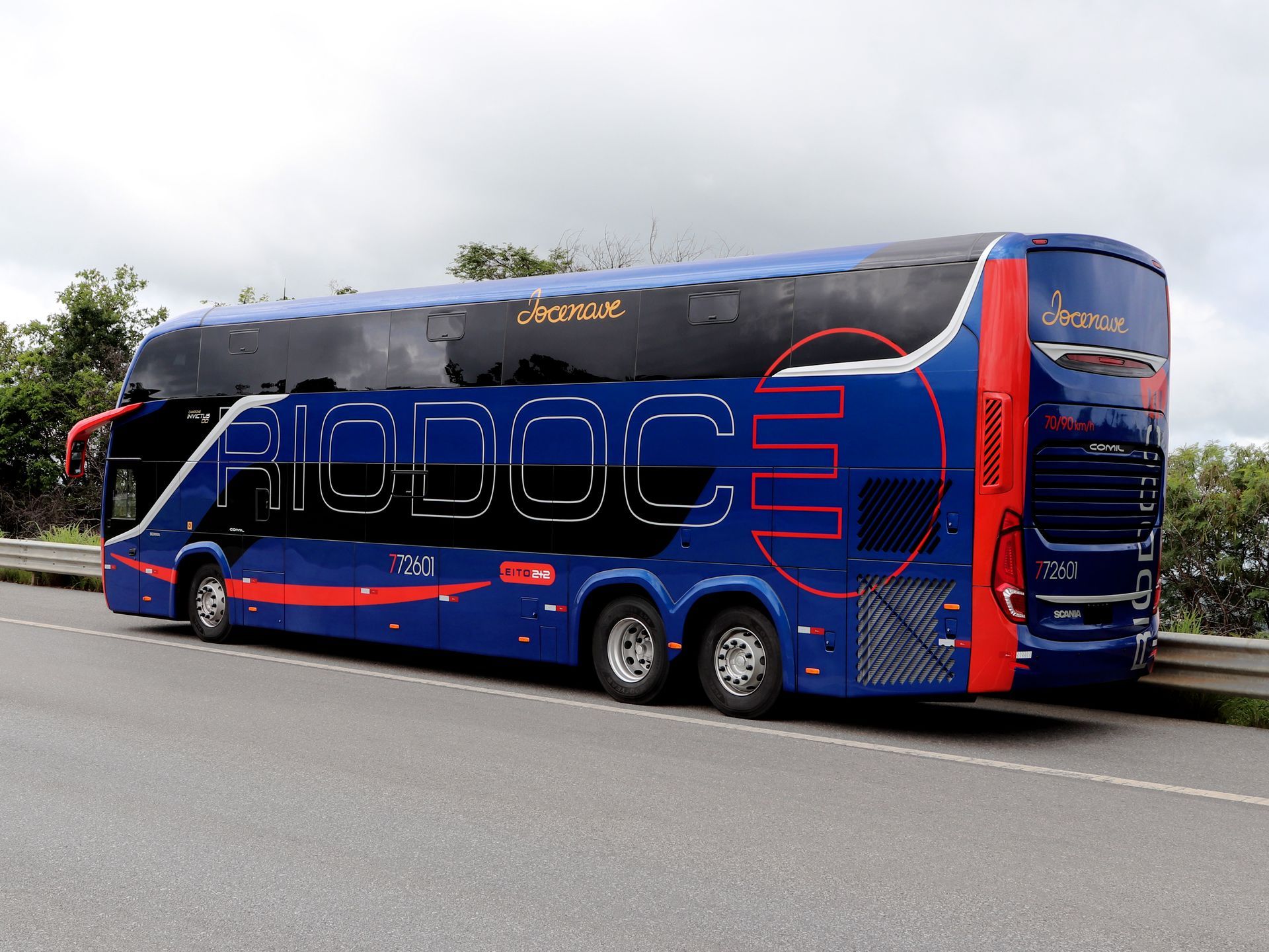 Um ônibus azul de dois andares da Riodoc estacionado na beira de uma rodovia contra um céu nublado.