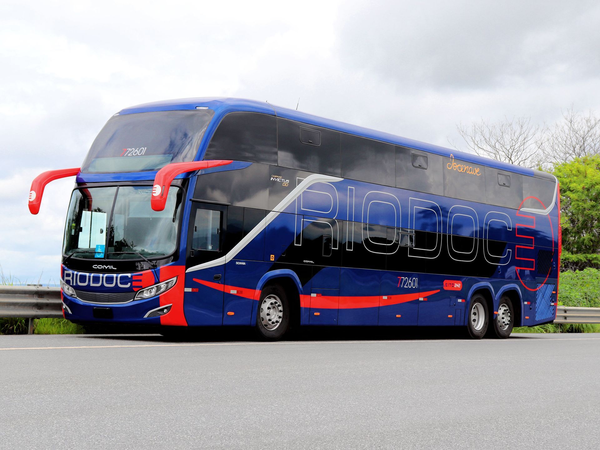 Um ônibus azul de dois andares com detalhes em vermelho está estacionado na beira da estrada sob um céu nublado.