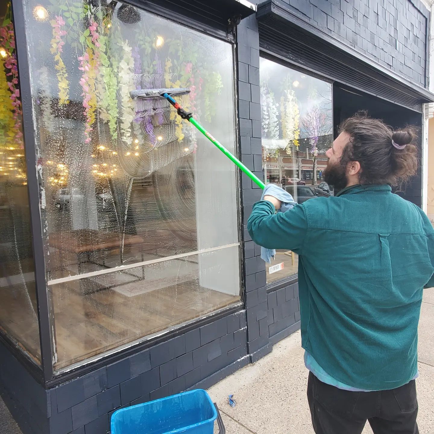 A man is cleaning a window with a green brush.