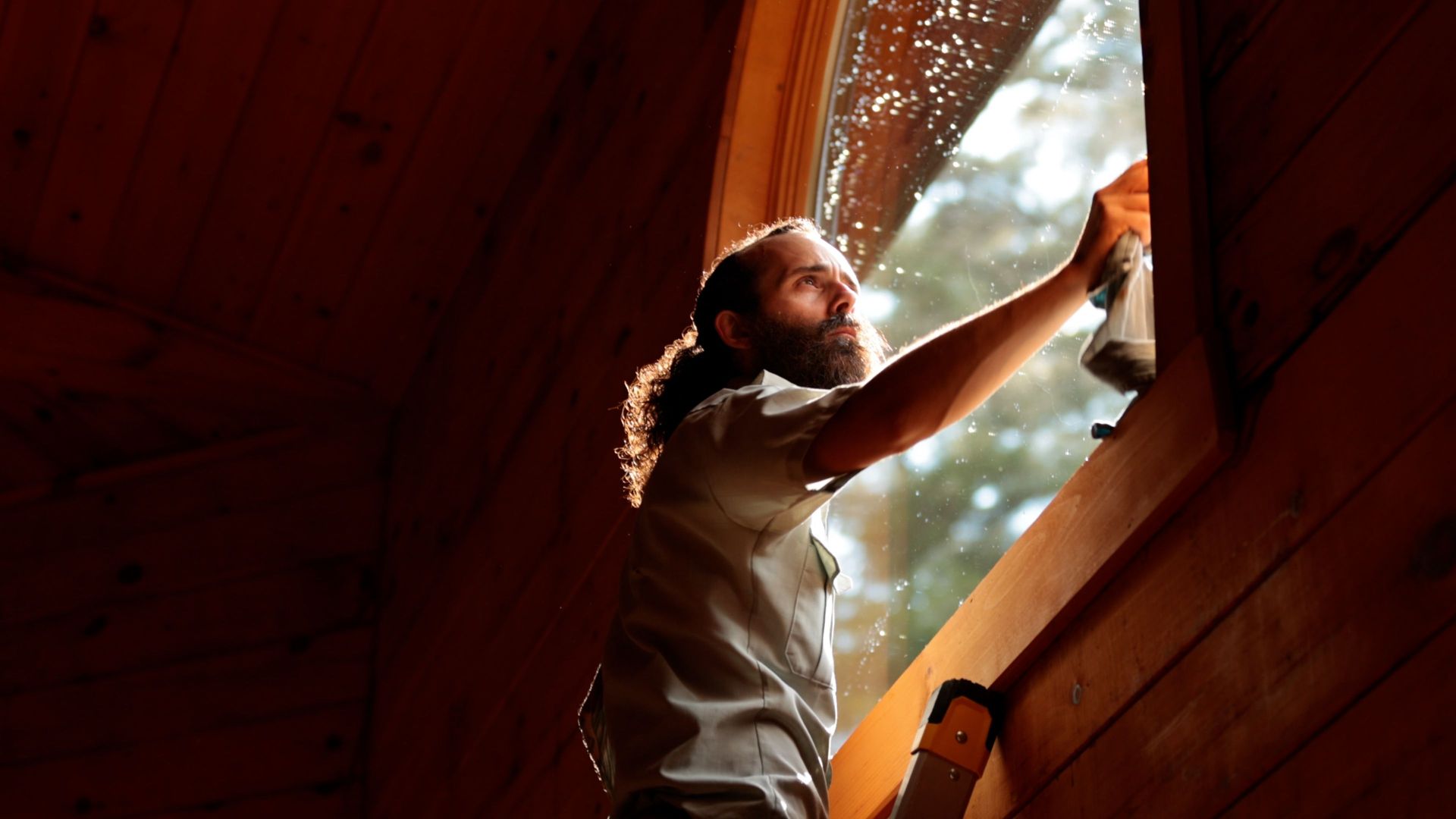 A man is standing on a ladder cleaning a window.