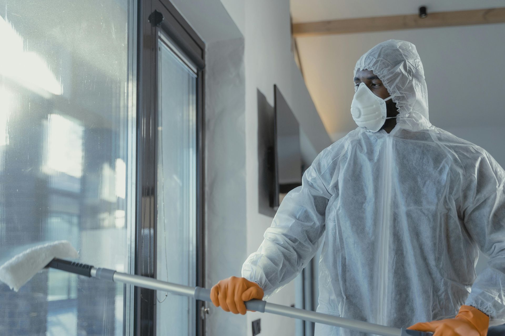 Person in hazmat suit cleaning window indoors with a squeegee.