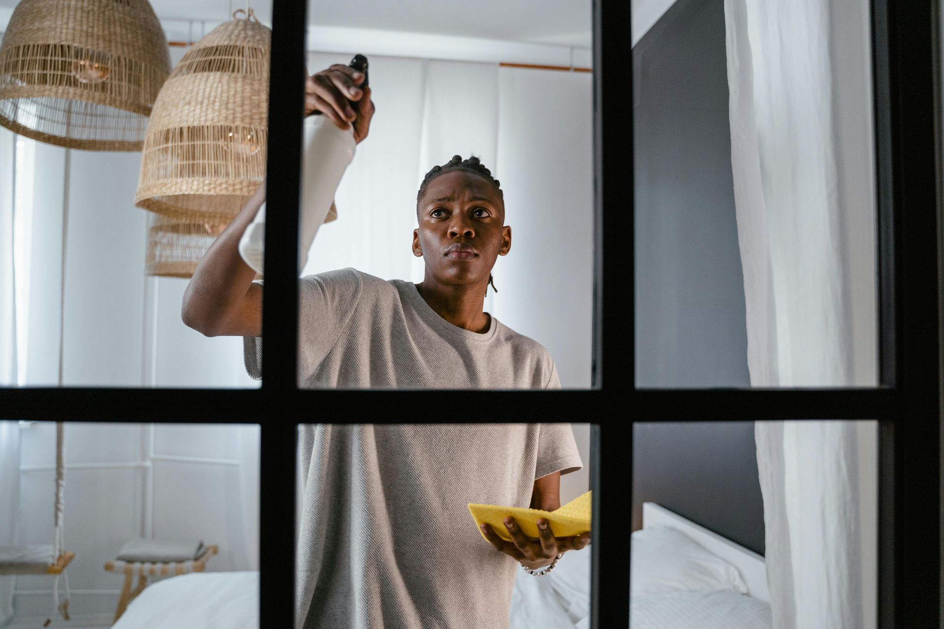 A man is cleaning a window with a sponge in a bedroom.