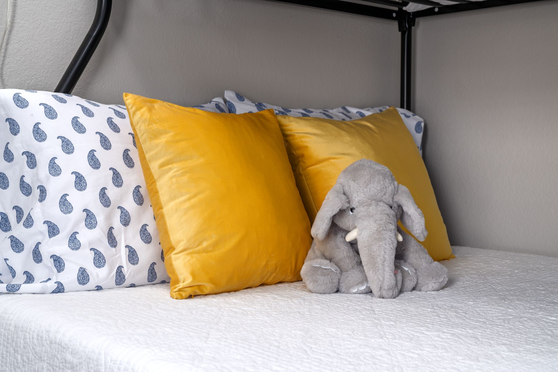 A stuffed elephant toy sitting on a bed with yellow and patterned pillows in a cozy nook.