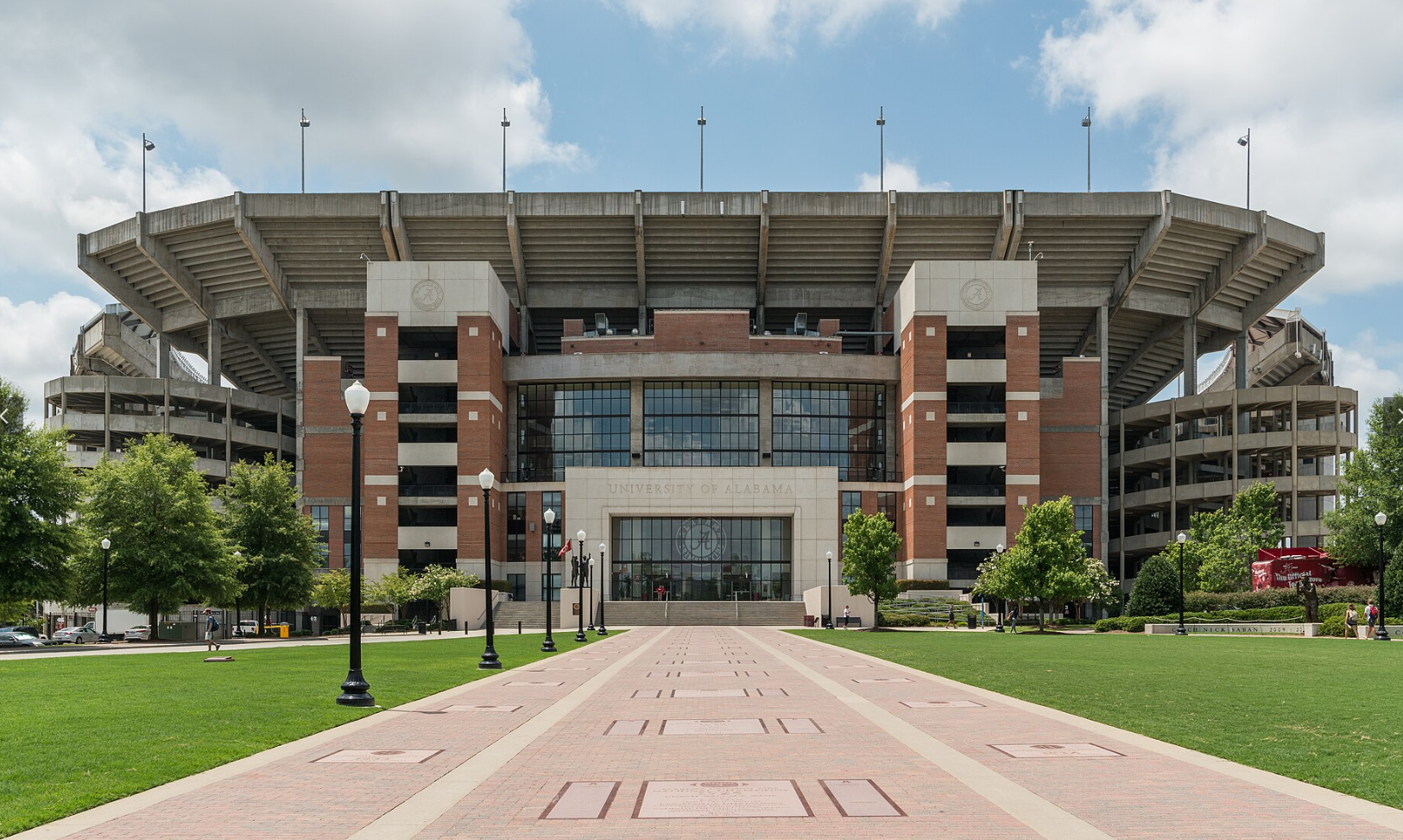 Stadium with a brick and concrete facade, walkway leading to the entrance, blue sky.