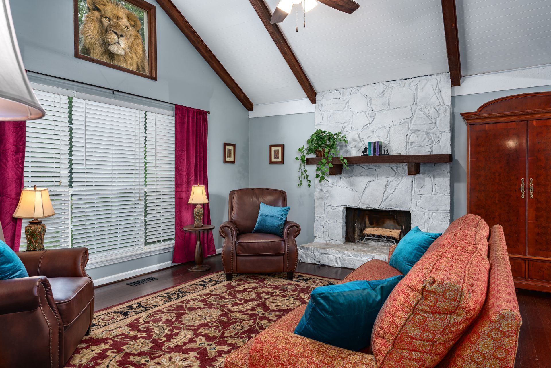 Cozy living room with vaulted ceiling, fireplace, leather chairs, patterned rug, and red curtains