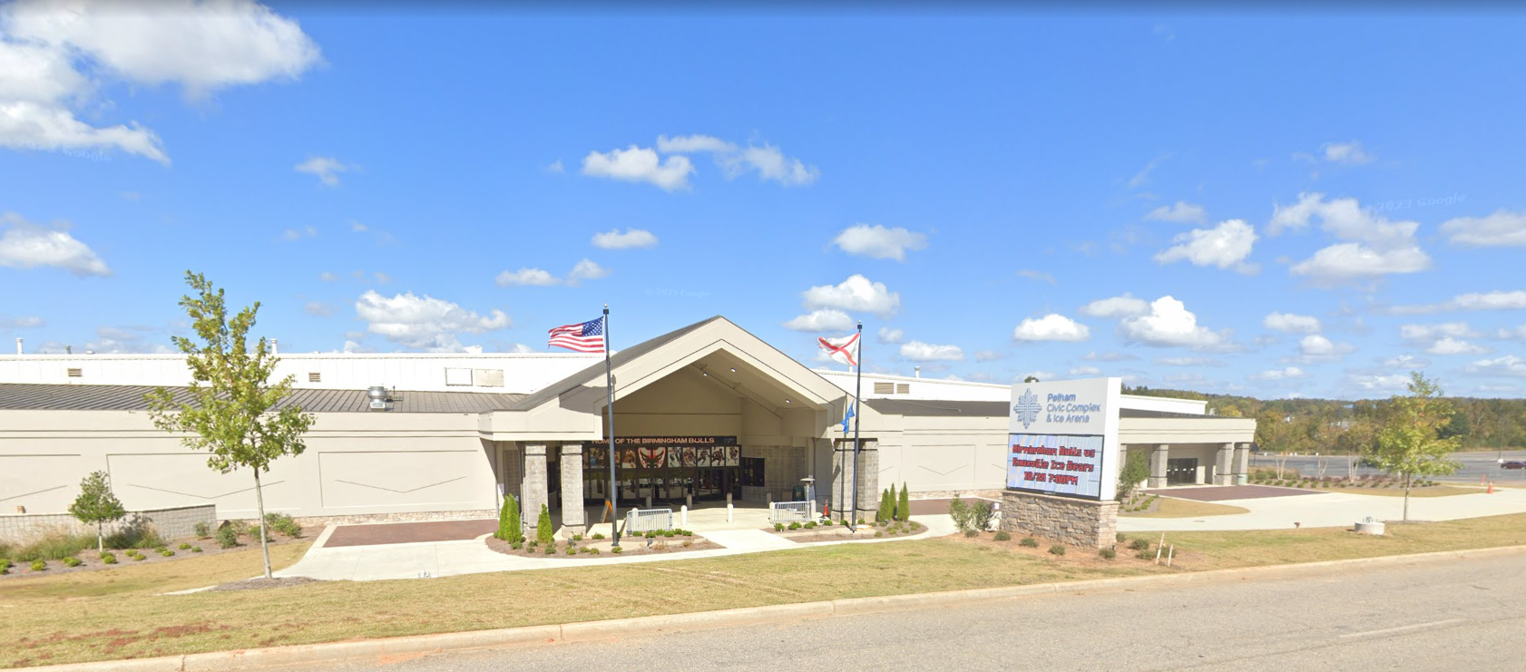 Building with a covered entrance, flags, and a sign on a sunny day.